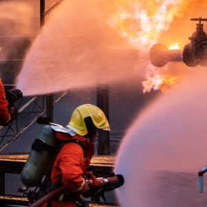 Panoramic Firefighter team use water fog type fire extinguisher to fight with flame from oil pipeline leak and explosion on oil rig and natural gas station. Firefighter and industrial safety concept.