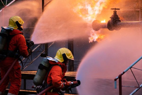 Panoramic Firefighter team use water fog type fire extinguisher to fight with flame from oil pipeline leak and explosion on oil rig and natural gas station. Firefighter and industrial safety concept.